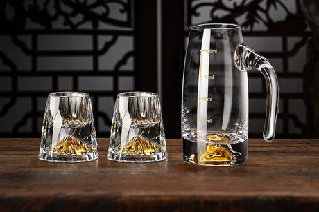 Set of clear glassware with gold accents on a wooden surface against a dark decorative wall.