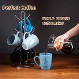 Coffee maker with mugs and a person pouring coffee into a blue mug on a wooden surface.