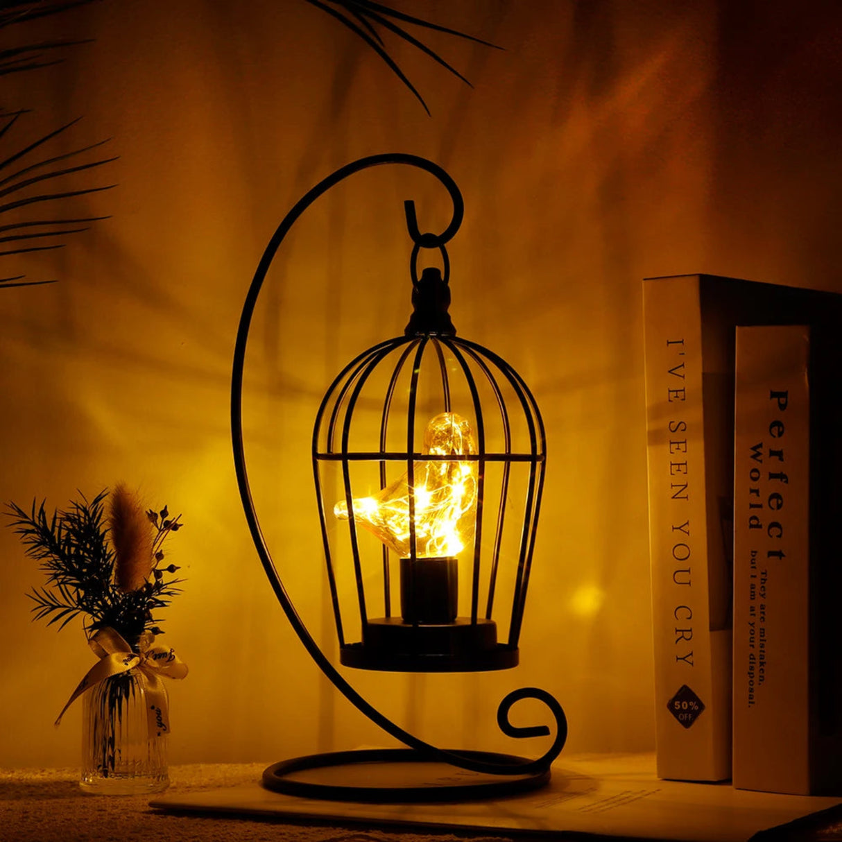 Decorative metal lantern with a candle inside, placed on a surface with books and a plant in the background.
