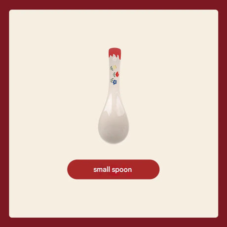 White ceramic spoon with floral design on a red handle against a beige background