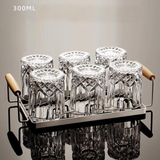 Set of six clear glass tumblers with wooden handles on a metal tray against a neutral background.