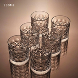 Set of six patterned glass tumblers on a reflective surface with a beige background.