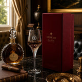 Louis XIII cognac liqueur bottle with a crystal decanter, a coupe glass, and a deep burgundy presentation box on a dark marble table in an elegant room setting.
